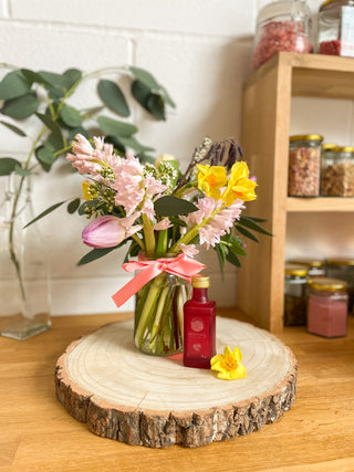 Jar of spring seasonal flowers sits on shelf. A mini bottle of gin is infront of the flowers.