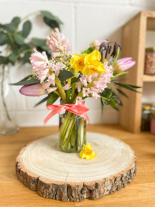 A jar of spring flowers sits on top of shelf.